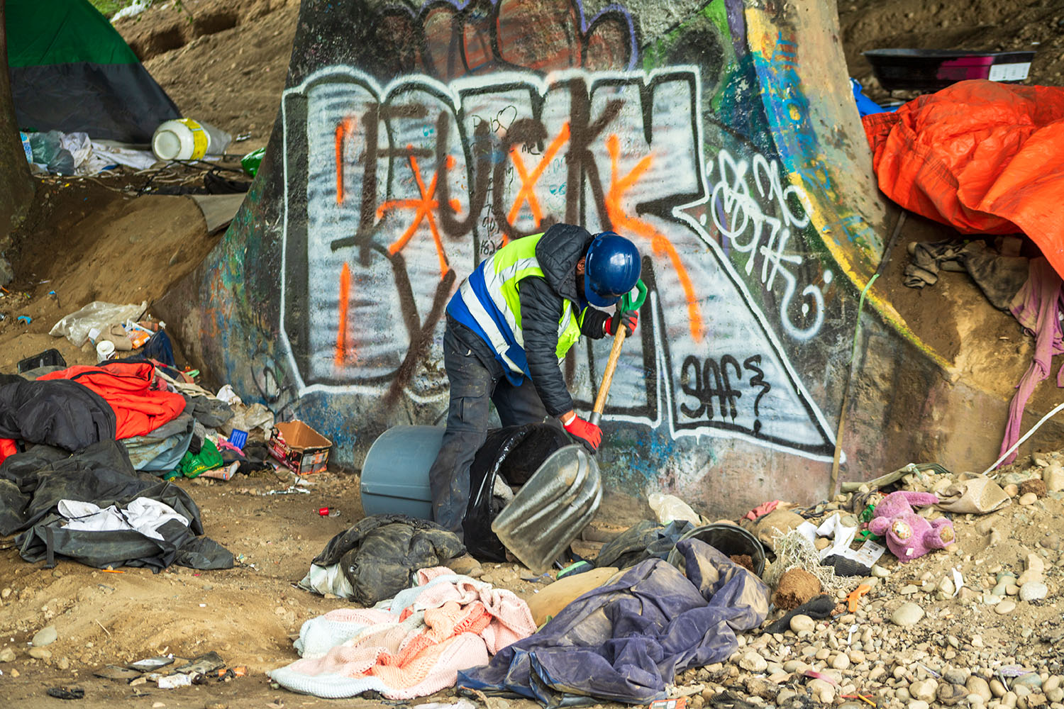A Recycle It Canada crew man with a shovel clearing a homeless encampment site filled with clothes and debris