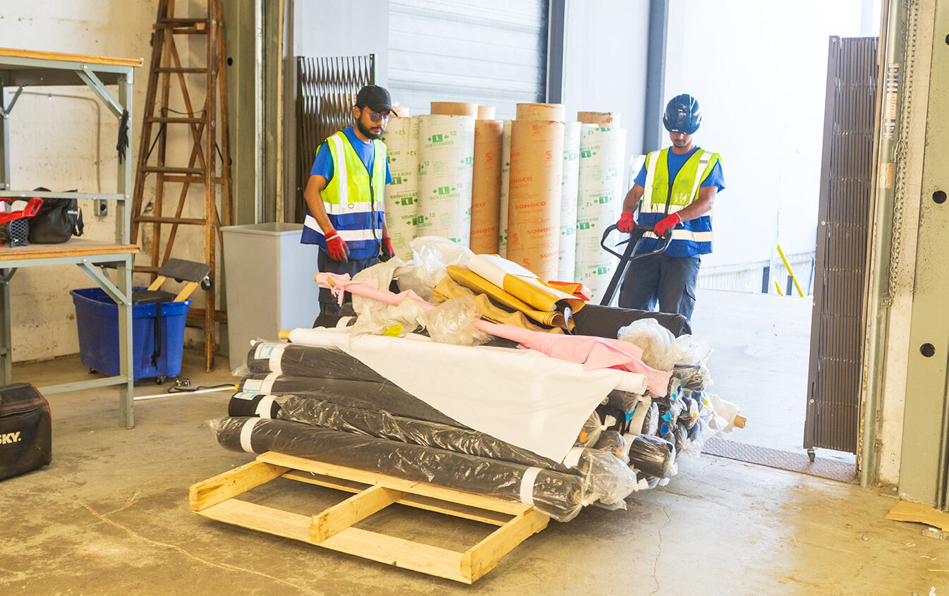 Two Recycle It Canada crew in front of a warehouse pulling a paleet of unused fabric rolls